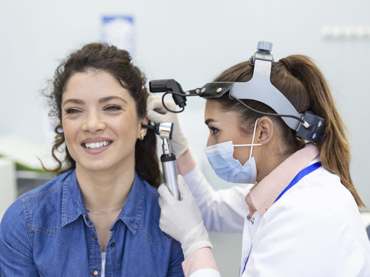 Hearing exam. Otolaryngologist doctor checking woman's ear using otoscope or auriscope at medical clinic.